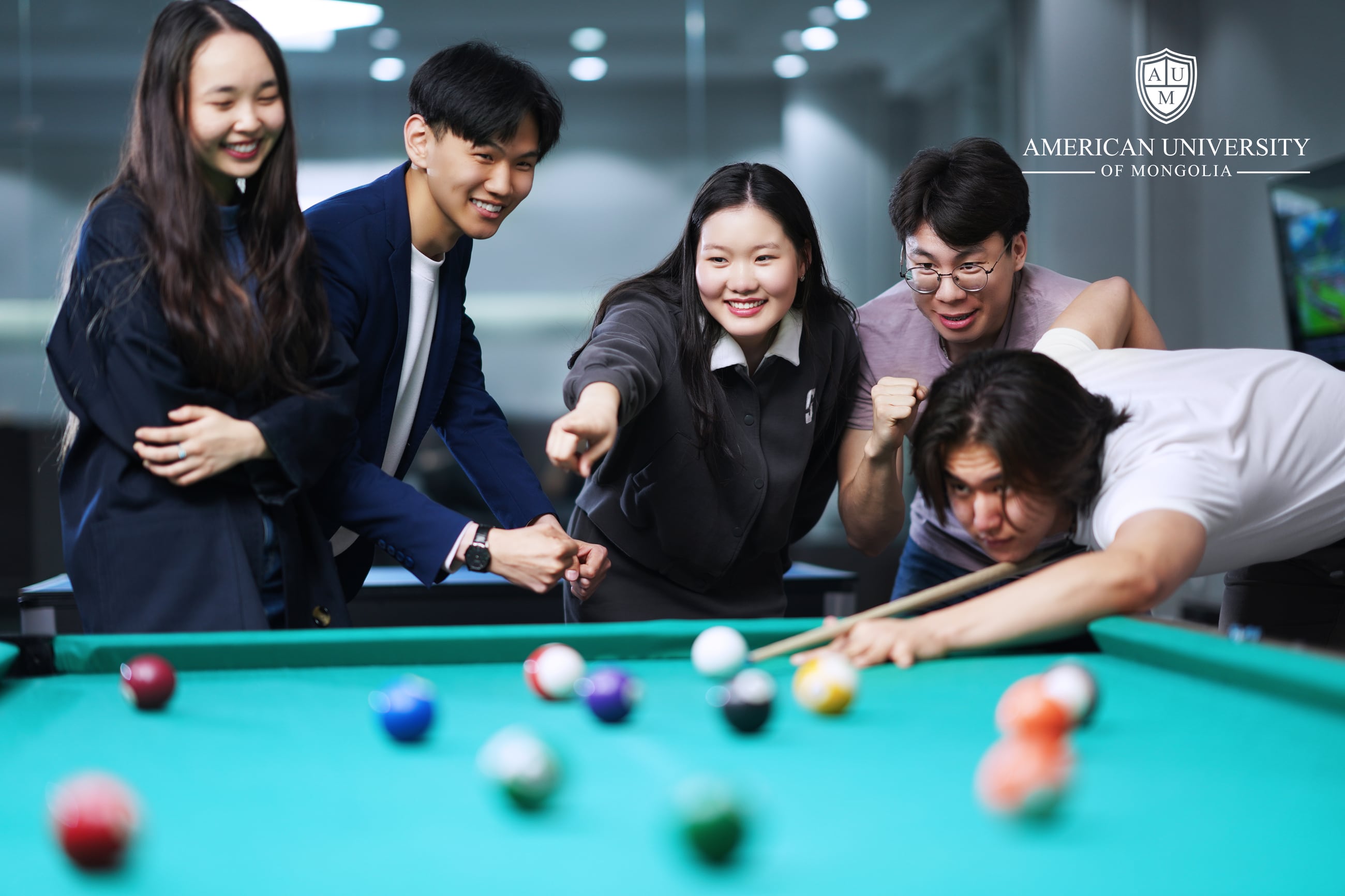AUM students gathered around a pool table with the university logo on the wall